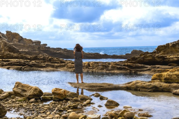 Woman standing on a natural rock formation, looking out at the rugged jaizkibel coast and atlantic