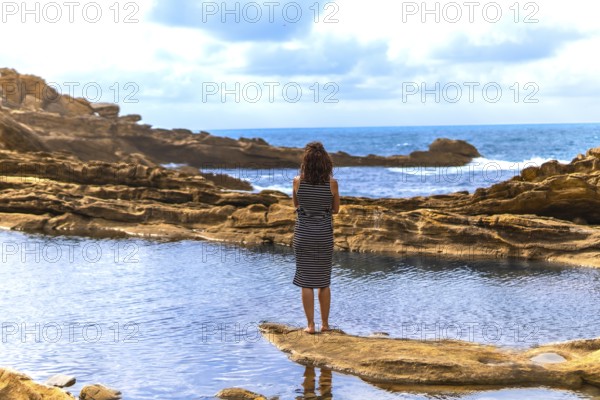 Woman standing barefoot on a rocky outcrop, observing the vast sea and dramatic sky, finding a