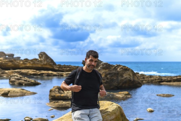 Man with a beard and backpack standing on coastal rocks by the sea, exploring the unique geological