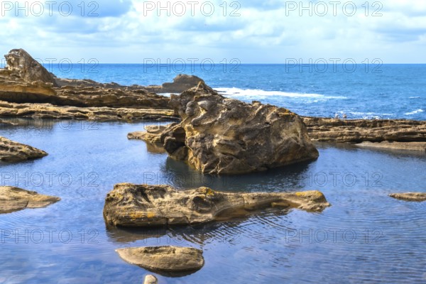 Rocky coastline creating natural tide pools and textured rock formations, showcasing geological