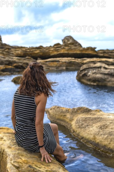 Woman sitting on coastal rock formations, enjoying the calm water and rugged landscape of