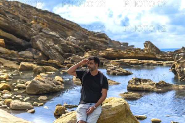 Man in outdoor clothing and backpack exploring a rugged coastal area with geological formations and