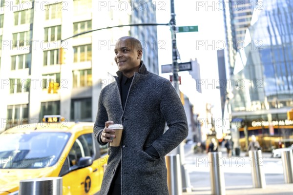 Confident black professional in smart casual coat holding a takeaway coffee cup, walking a busy