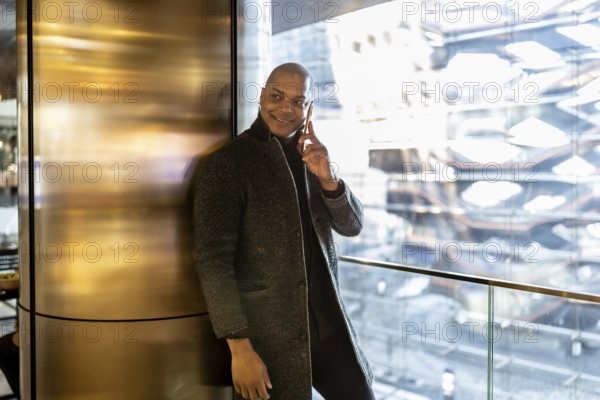 Black businessman standing in a modern building with city views, engaged in a phone call and