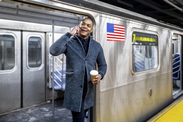 Smiling young professional holding a coffee and talking on his smartphone while stepping off a