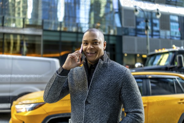 Smiling businessman making a phone call, standing on a busy street in manhattan with cars and