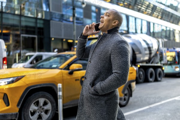 Young professional in a coat making a phone call while walking through a busy manhattan street with