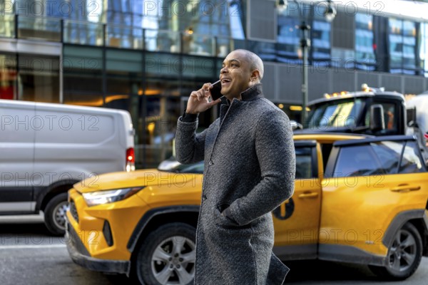 Happy professional businessman talking on a mobile phone, standing on a bustling urban street with