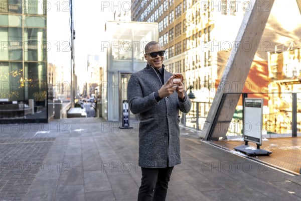 Happy professional man walking and using a smartphone in a bustling manhattan street environment,