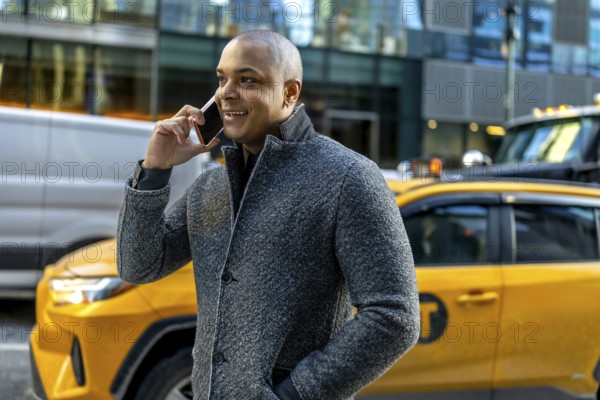 Busy professional man in a winter coat smiling and talking on his smartphone while walking through