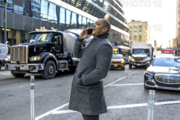 Smiling businessman talking on his mobile while walking a busy manhattan street, illustrating urban