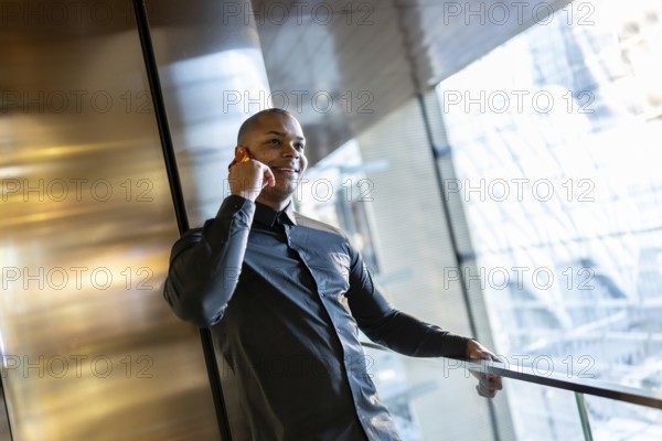 Smiling young professional man is confidently speaking on his cell phone while leaning on a railing