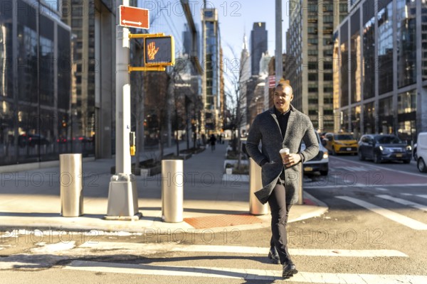 Young businessman walking confidently across a crosswalk in manhattan with a coffee cup, showcasing
