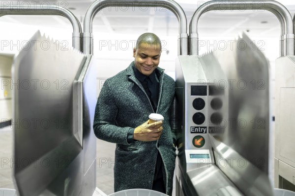 Young professional passing a manhattan subway turnstile with a takeaway coffee, entering the metro