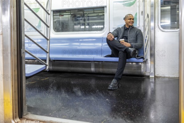 Man smiling and enjoying coffee while traveling on an empty subway car, reflecting daily commute,