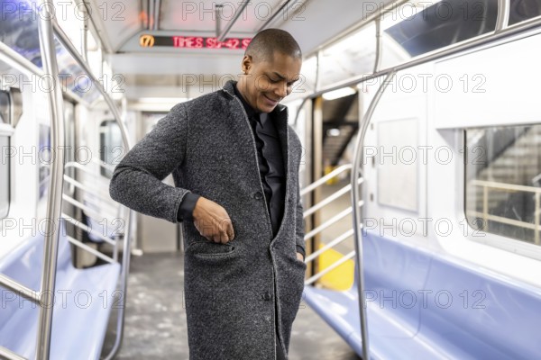 Young professional standing in a manhattan subway car, smiling as he adjusts his coat pocket, ready