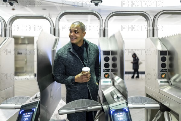 Professional man carrying a coffee cup, about to enter the subway system through modern turnstiles,