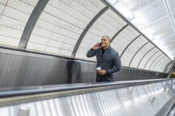 Businessman navigating urban commute on an escalator while engaged in a mobile phone conversation,