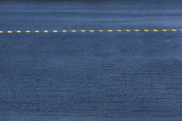 String of yellow cautionary navigation marker buoys on water surafce of river serving to warn,