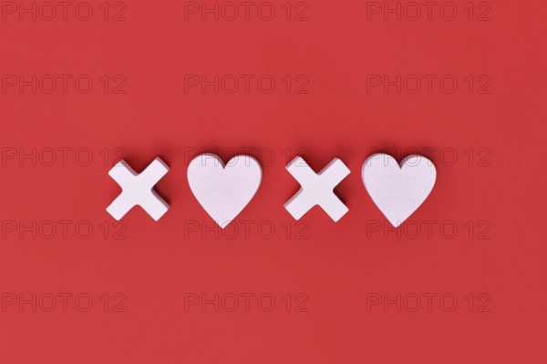 Valentine flat lay with wooden light pink hearts and XOXO letters arranged on a red background.