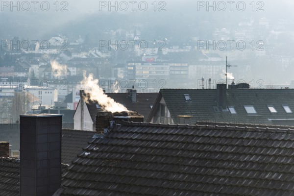 Smoke plume from a chimney over densely built residential area in the evening light, wintry city