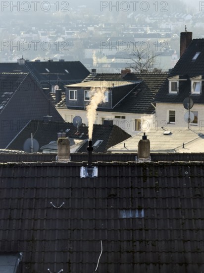 Smoke plume from a chimney over densely built residential area in the evening light, wintry city