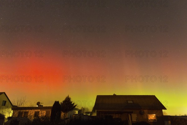 Red and green polar lights shine over houses, illuminated night sky, aurora borealis, Ilsede, Lower