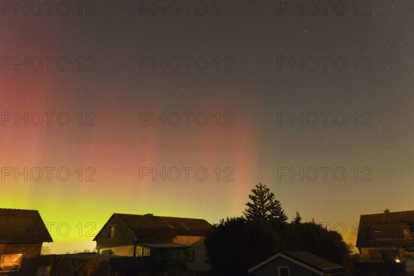 Red and green aurora borealis in the night sky above houses, trees silhouetted, aurora borealis,