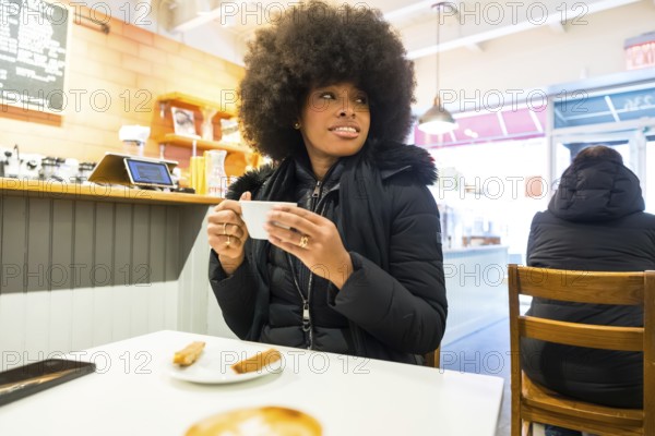 Young african american woman relaxing in a cozy manhattan coffee shop, enjoying a hot coffee during