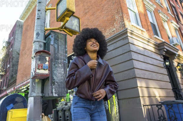 Young african american woman with afro hair smiling and looking up, walking in a vibrant new york