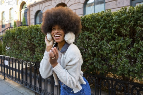 Young african american woman with an afro hairstyle laughing brightly, wearing warm earmuffs and a