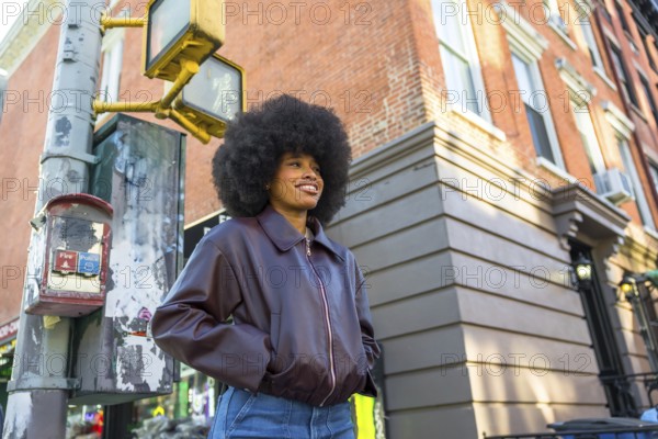 Young woman smiling while standing confidently on a new york city street corner, featuring an afro