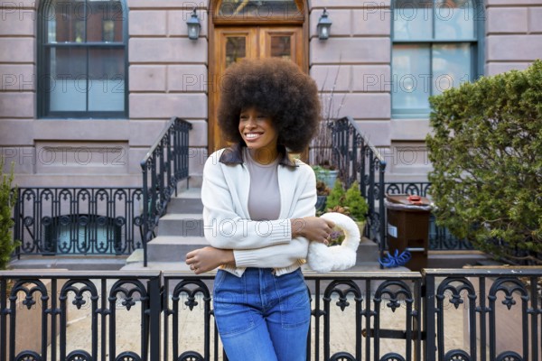 Smiling young woman with a large afro hairstyle and fashionable attire standing in front of a