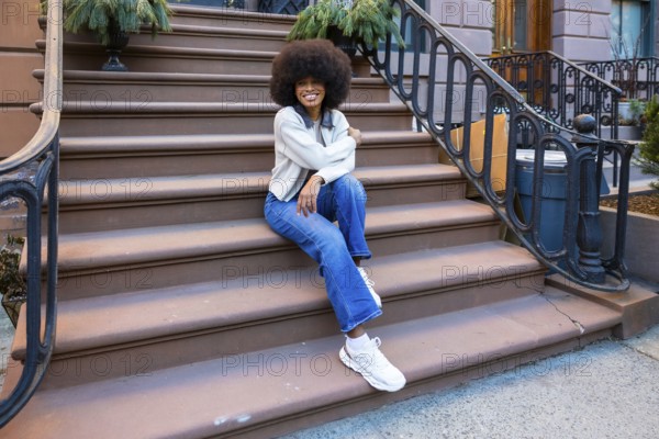 Young african american woman with afro hair sitting on a brownstone stoop in a new york city