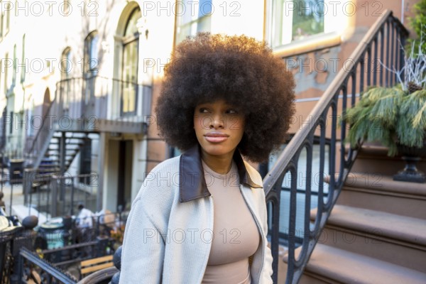 Young african american woman with voluminous afro hair standing on the steps of a brownstone