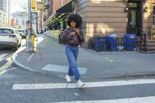 Young woman with afro hair and casual fashion attire confidently walking across a zebra crossing in