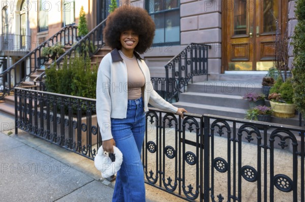 Young black woman with a large afro in jeans and a sweater, smiling confidently while standing on a