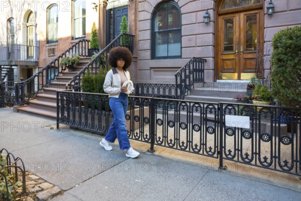 Young woman with afro hair walking down a sidewalk in a historical new york city neighborhood,