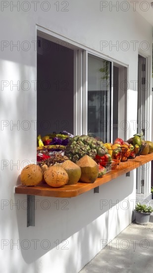 Assortment of fresh tropical fruit and young raw coconuts displayed on a wooden shelf outside a