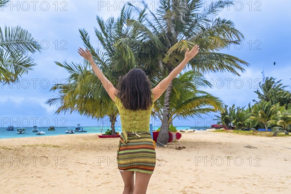 Woman standing on a white sand beach, raising arms to the sky, embracing joy and freedom during a