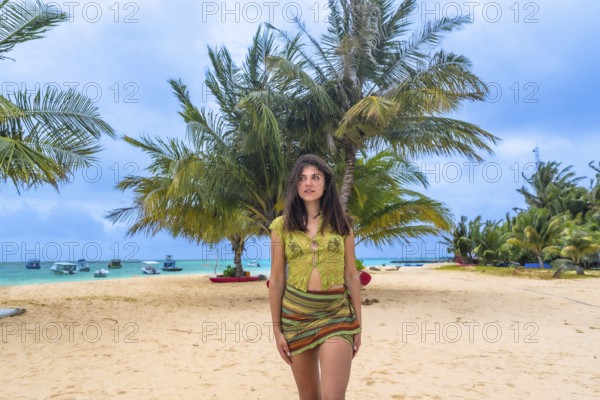 Woman standing on a sandy beach looking out towards the turquoise ocean, surrounded by lush palm