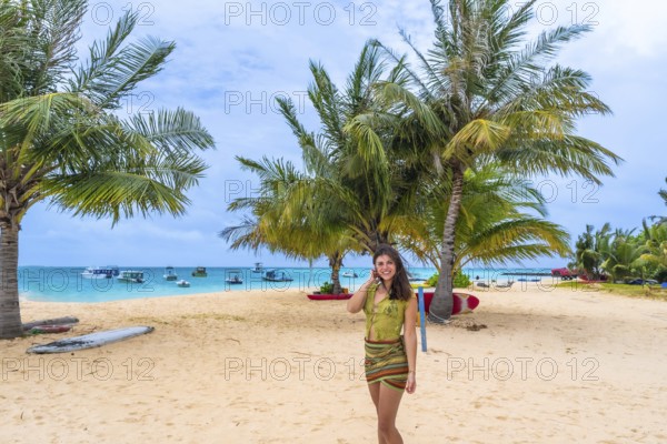 Woman smiling and standing on a beautiful sandy beach fringed with green palm trees and turquoise