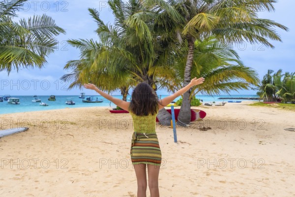 Woman standing on a tropical sandy beach with arms outstretched, experiencing a joyful moment of