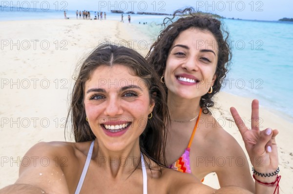 Smiling women capturing a joyful selfie on a beautiful white sand beach with turquoise water during