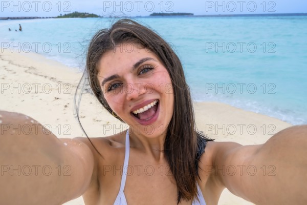 Woman smiling for a selfie on a white sand maldivian beach, embracing sunny tropical vacation vibes
