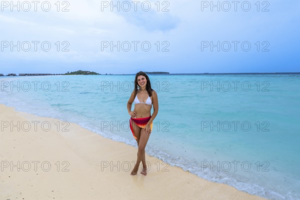 Young woman smiling while standing on a pristine sandy beach with turquoise ocean water, enjoying a