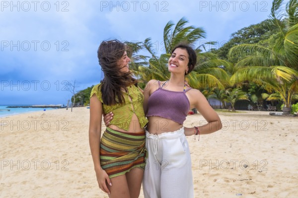Young women friends embracing on a sunny tropical beach, smiling and enjoying a relaxing island