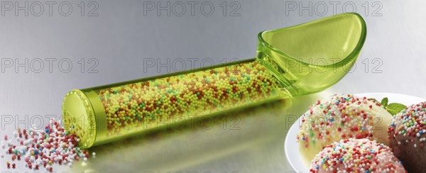 Yellow, transparent ice cream scoop filled with coloured sugar sprinkles, next to a plate with