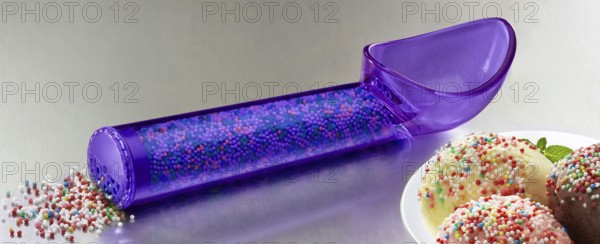 Purple, transparent ice cream scoop filled with coloured sugar sprinkles, next to plates with