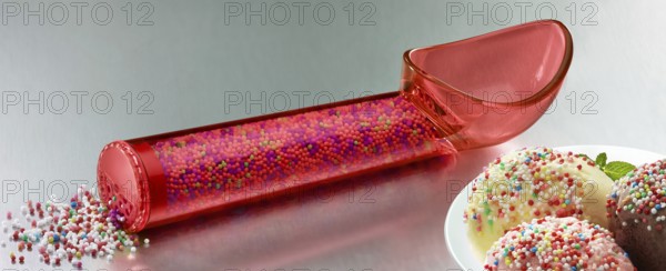 Red, transparent ice cream scoop filled with coloured sugar sprinkles, next to a plate with